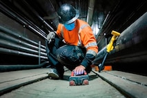 A contractor wearing a face mask kneels down to use a tool.