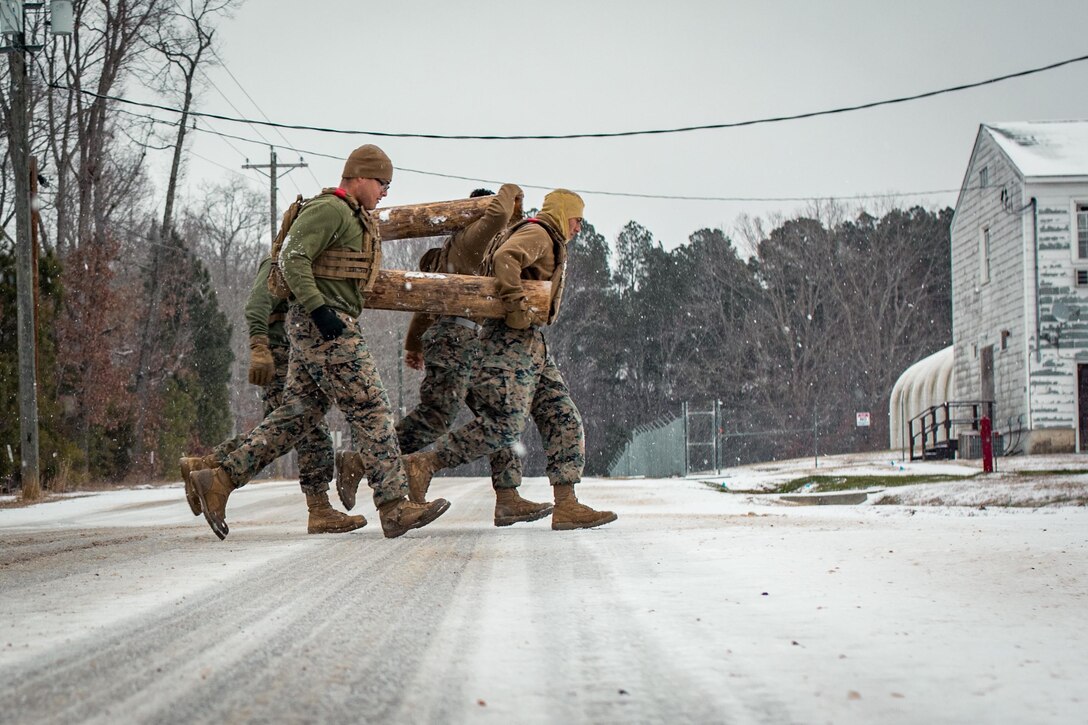 Marines carrying logs run through the snow.