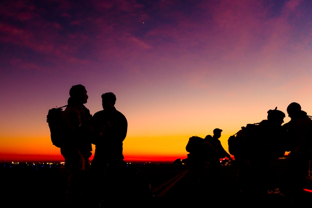 Airmen speak to each other under a sunlit sky as shown in silhouette.