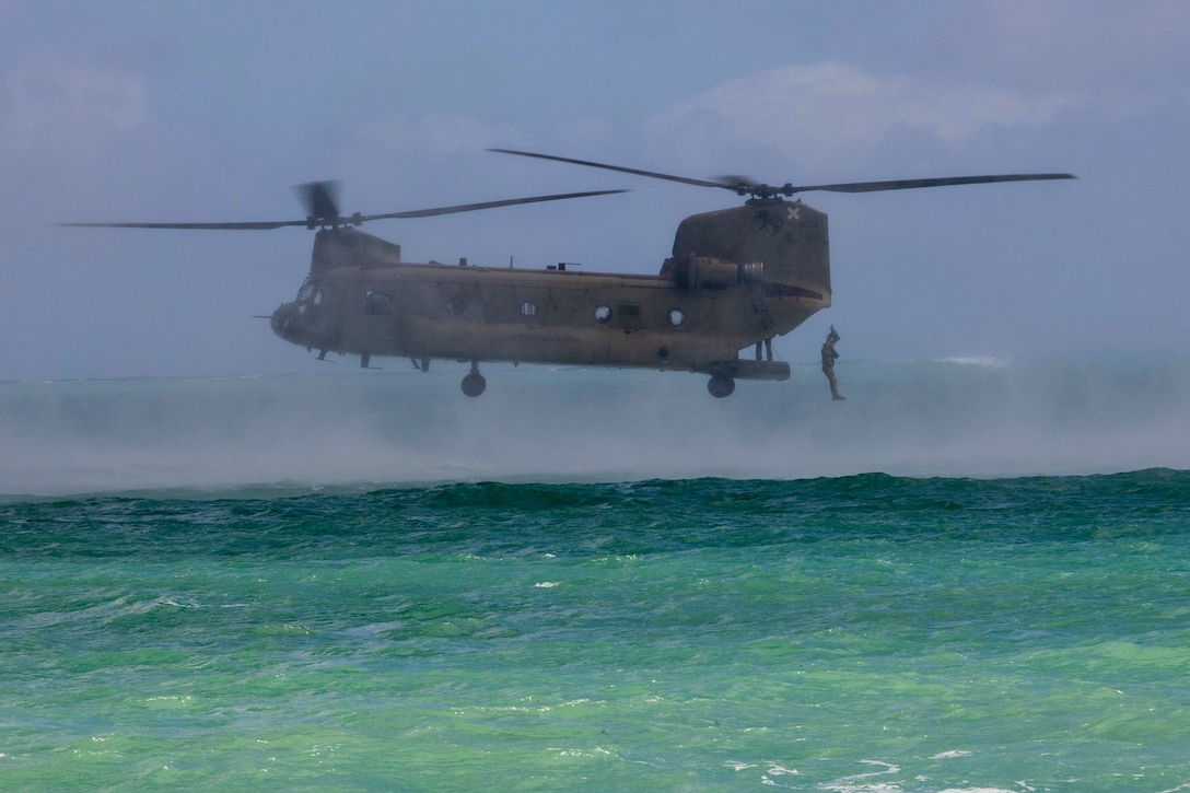 A soldier jumps from an airborne helicopter into a body of water.