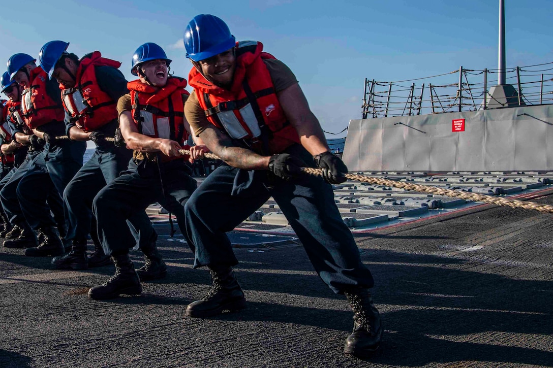 Sailors standing in a line pull a rope.