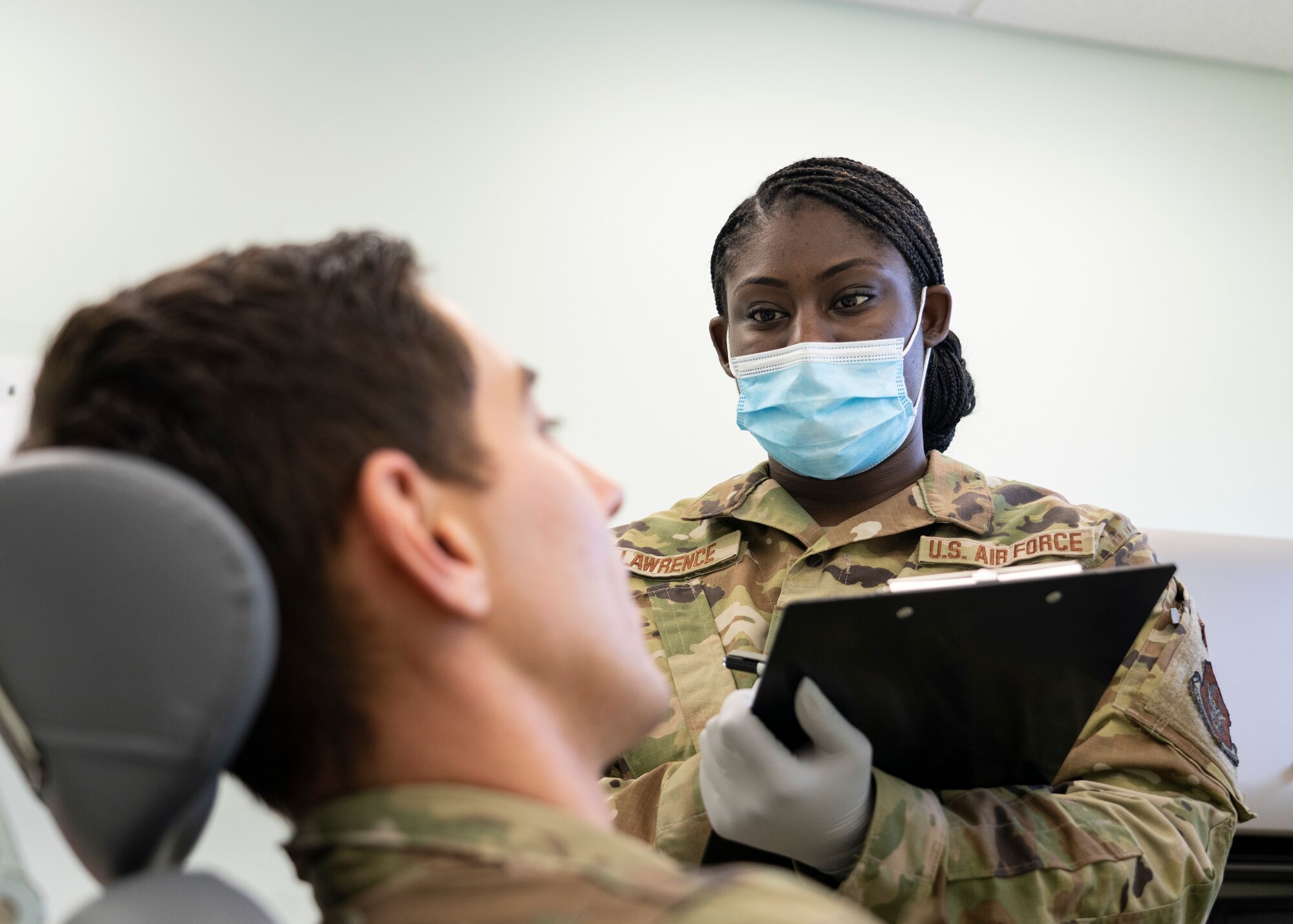 Airman with clipboard stands beside Airman in dental chair.
