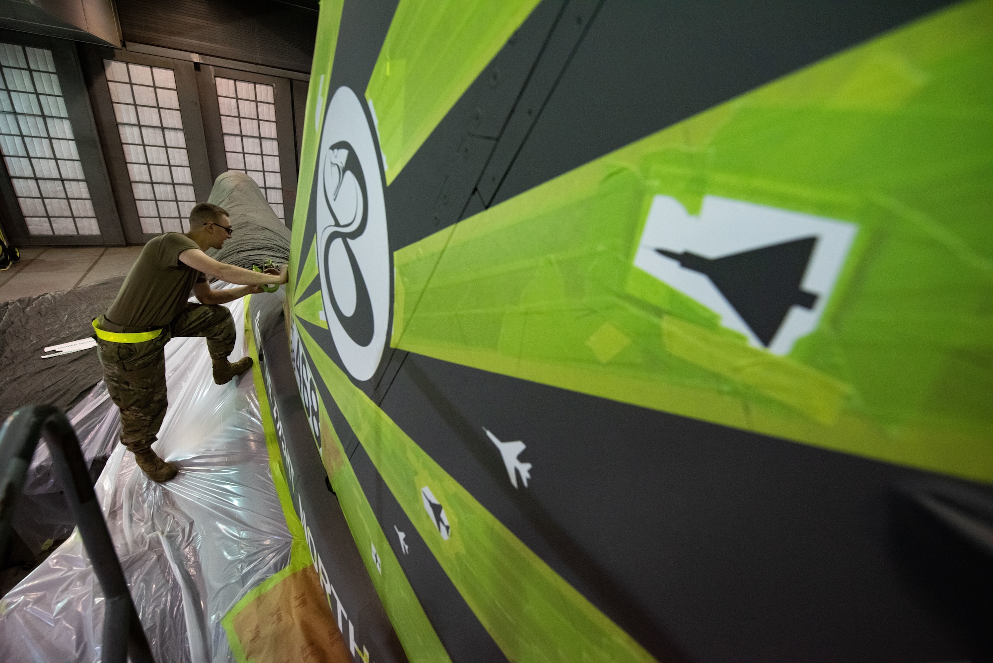 Senior Airman Ryan Slesser, 8th Maintenance Squadron aircraft structural maintenance journeyman applies masking tape to outline a tail flash design for an F-16 Fighting Falcon