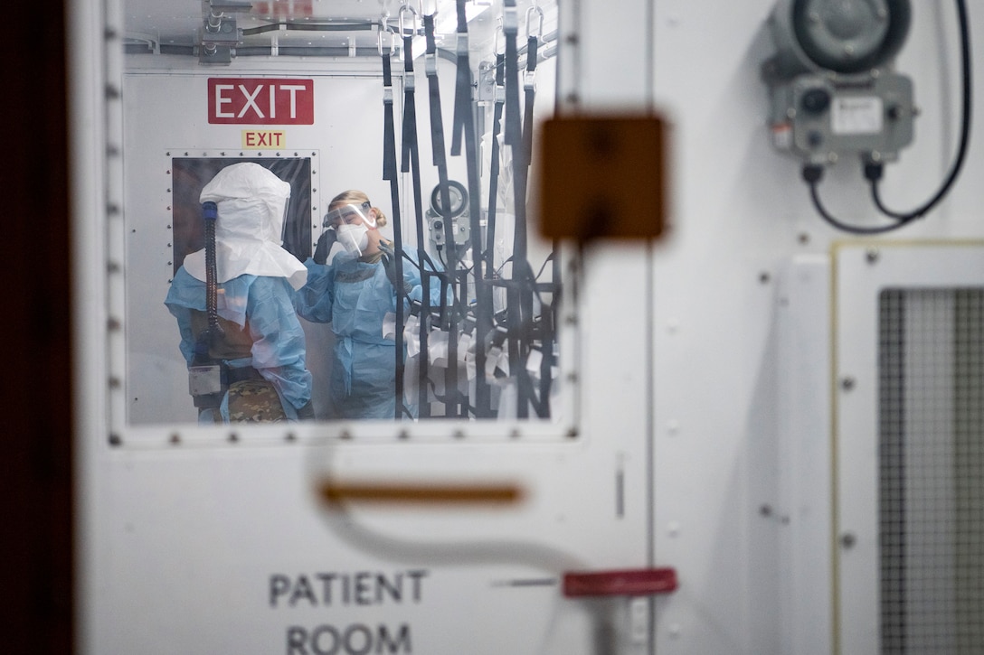 Two airmen wearing medical protective gear talk inside a container system.