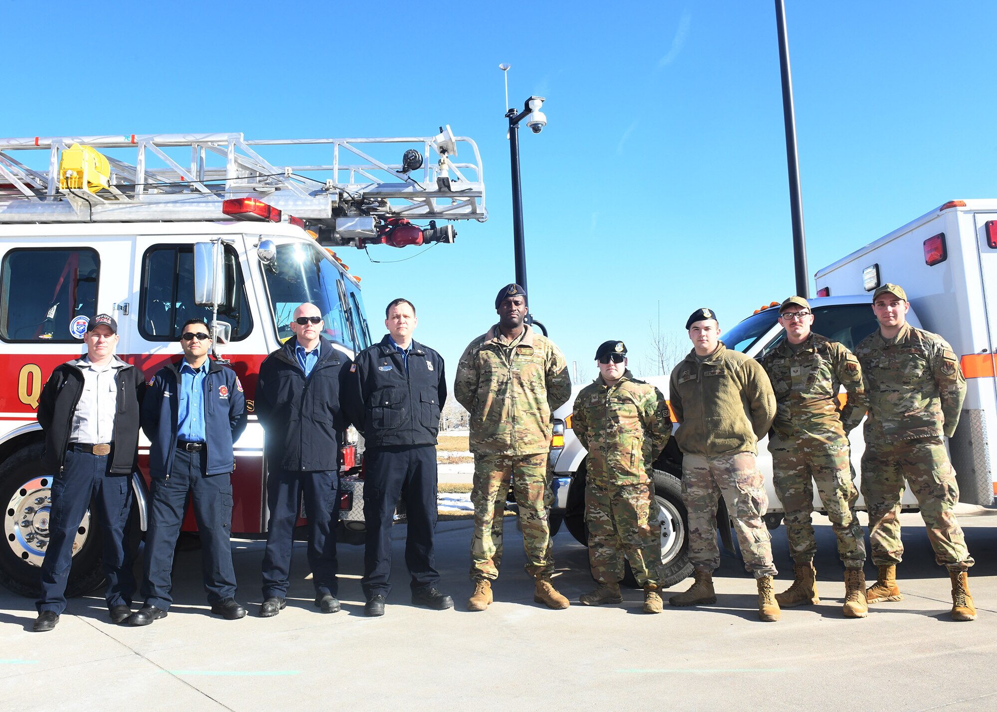 Group of first responders pose for photo in front of ambulance and fire truck.