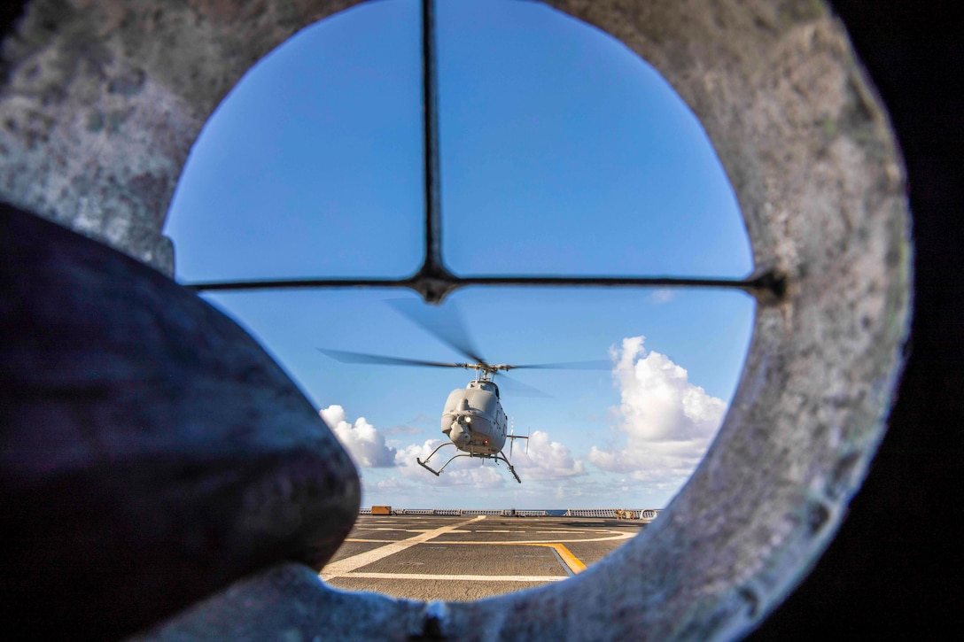 A helicopter seen through a porthole takes off from the deck of a ship.