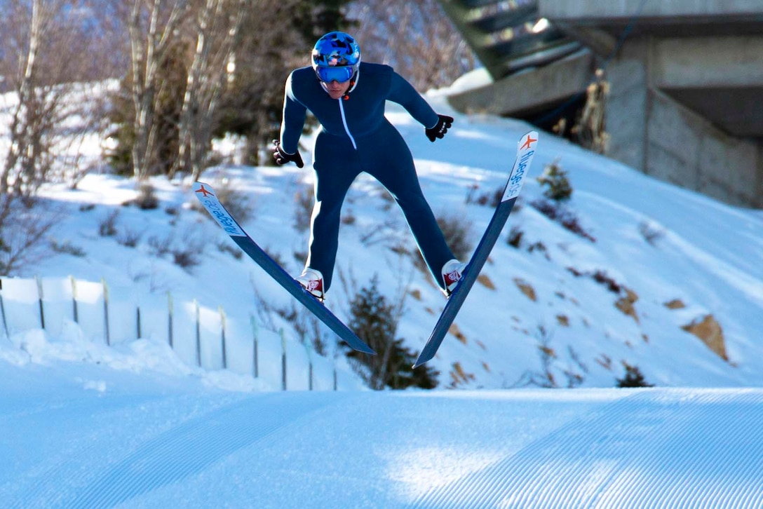 A guardsmen jumps in the air wearing skis.
