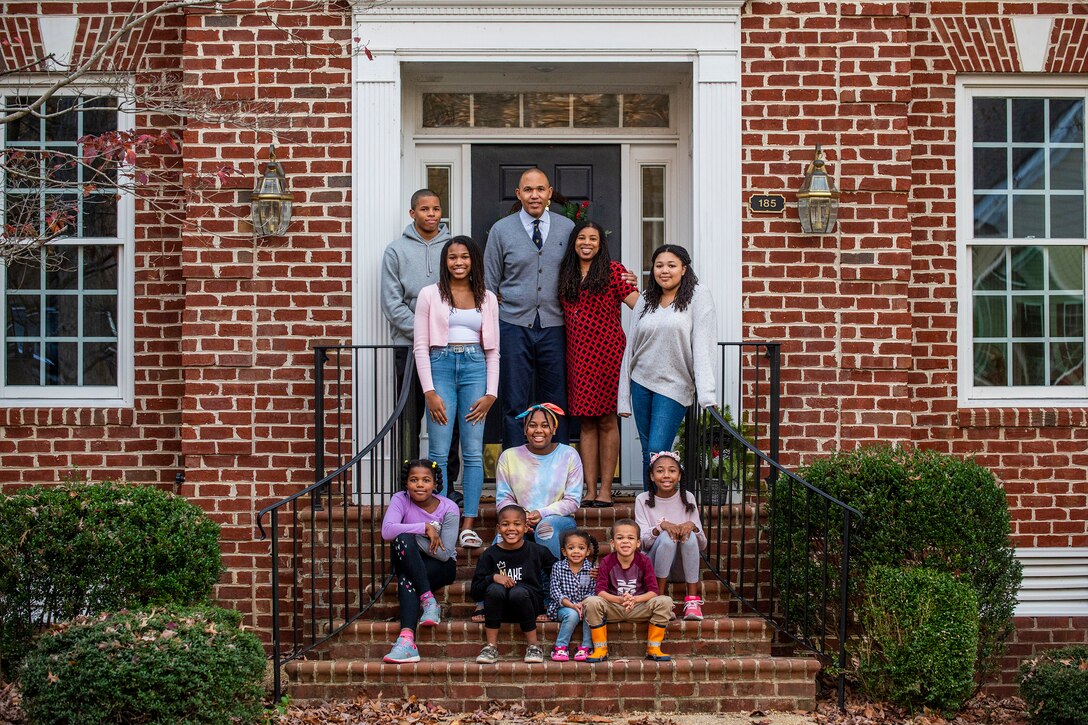 Two adults and nine youth of various ages pose for a photo on the steps of brick house.