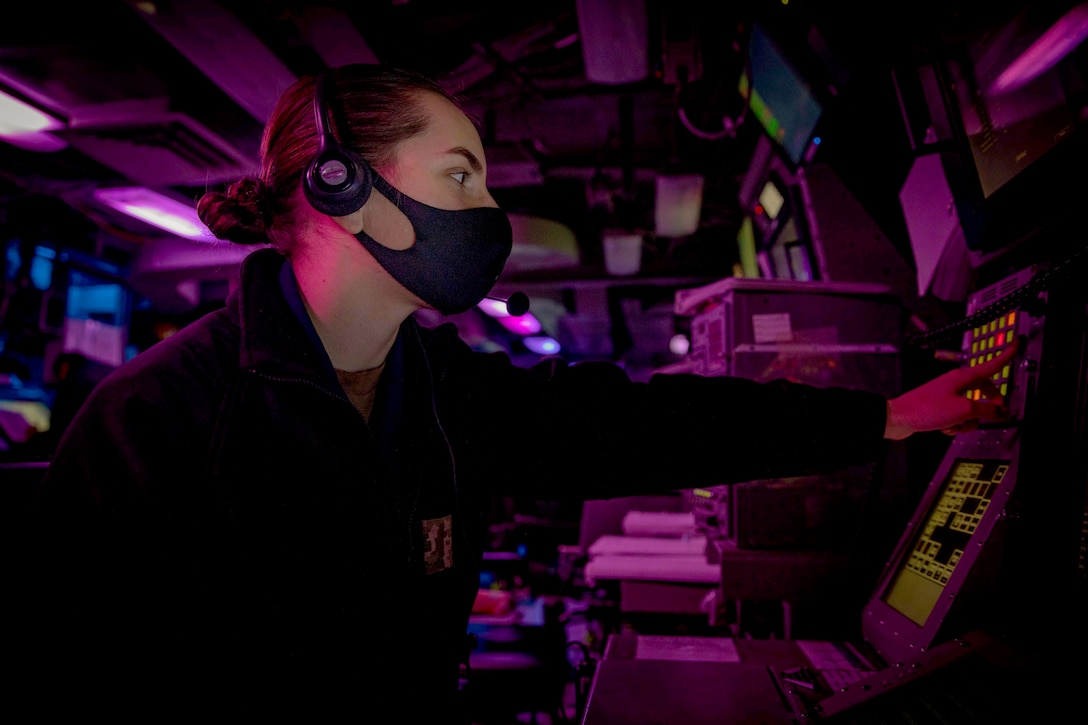 A sailor wearing a face mask touches controls in an information center.