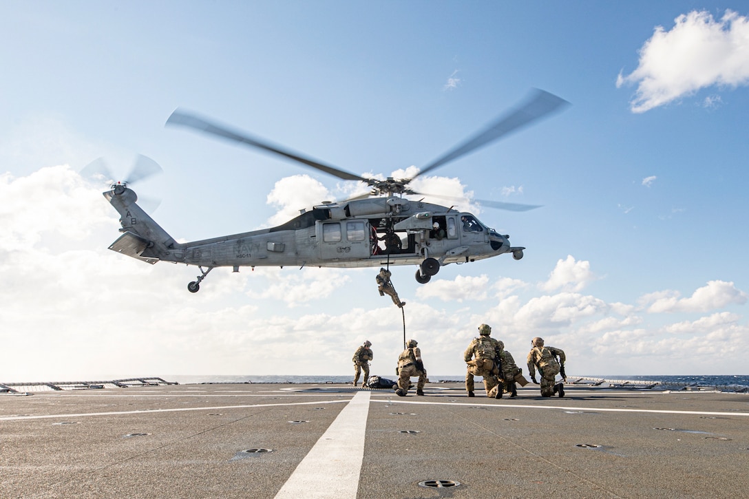 A sailor uses a rope to climb out of a helicopter hovering over a ship at sea.