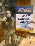 West Virginia Army National Guard Pvt. 1st Class Kristen Denny  stands inside a hospital lobby in military uniform and mask.