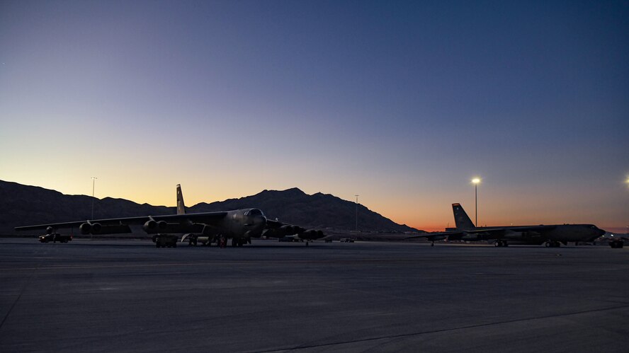 Two B-52s are parked on the runway at Nellis AFB at dusk