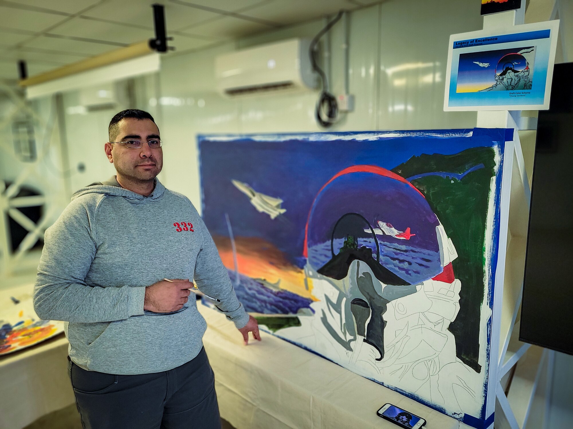 U.S. Air Force Brig. Gen. Christopher Sage, 332d Air Expeditionary Wing commander, center and Chief Master Sgt. Sean Milligan, command chief, right, stand with Senior Master Sgt. Fernando Buitrago, 332d Expeditionary Logistics Readiness Squadron senior enlisted leader inside the Red Tail Center of Excellence as they pose with the finished pieces of the Legacy Project, January 26, 2022, Southwest Asia.  The Legacy Project is a set of two paintings depicting the heritage and culture of the Tuskegee Airmen and the 332d AEW culture today, bringing past and present together. (U.S. Air Force photo by Master Sgt. Christopher Parr)