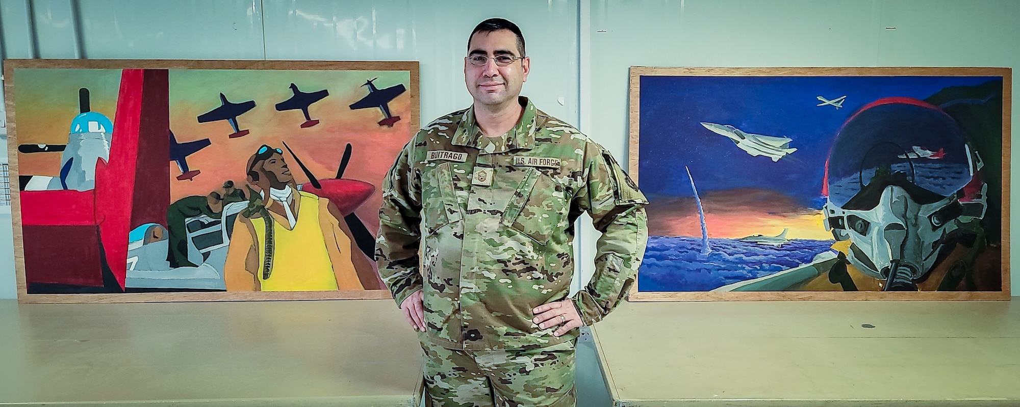 U.S. Air Force Brig. Gen. Christopher Sage, 332d Air Expeditionary Wing commander, center and Chief Master Sgt. Sean Milligan, command chief, right, stand with Senior Master Sgt. Fernando Buitrago, 332d Expeditionary Logistics Readiness Squadron senior enlisted leader inside the Red Tail Center of Excellence as they pose with the finished pieces of the Legacy Project, January 26, 2022, Southwest Asia.  The Legacy Project is a set of two paintings depicting the heritage and culture of the Tuskegee Airmen and the 332d AEW culture today, bringing past and present together. (U.S. Air Force photo by Master Sgt. Christopher Parr)