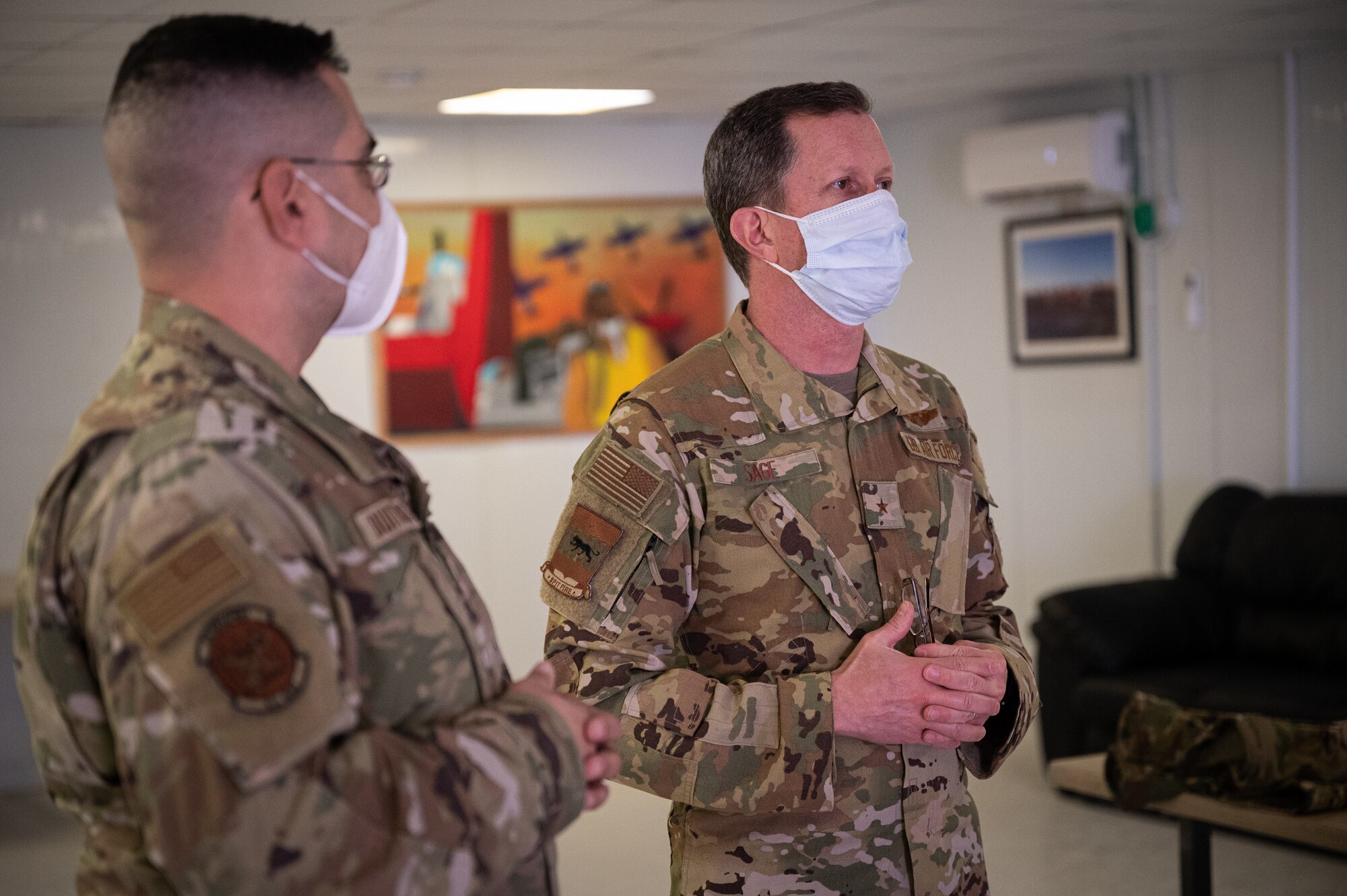 U.S. Air Force Brig. Gen. Christopher Sage, 332d Air Expeditionary Wing commander, center and Chief Master Sgt. Sean Milligan, command chief, right, stand with Senior Master Sgt. Fernando Buitrago, 332d Expeditionary Logistics Readiness Squadron senior enlisted leader inside the Red Tail Center of Excellence as they pose with the finished pieces of the Legacy Project, January 26, 2022, Southwest Asia.  The Legacy Project is a set of two paintings depicting the heritage and culture of the Tuskegee Airmen and the 332d AEW culture today, bringing past and present together. (U.S. Air Force photo by Master Sgt. Christopher Parr)