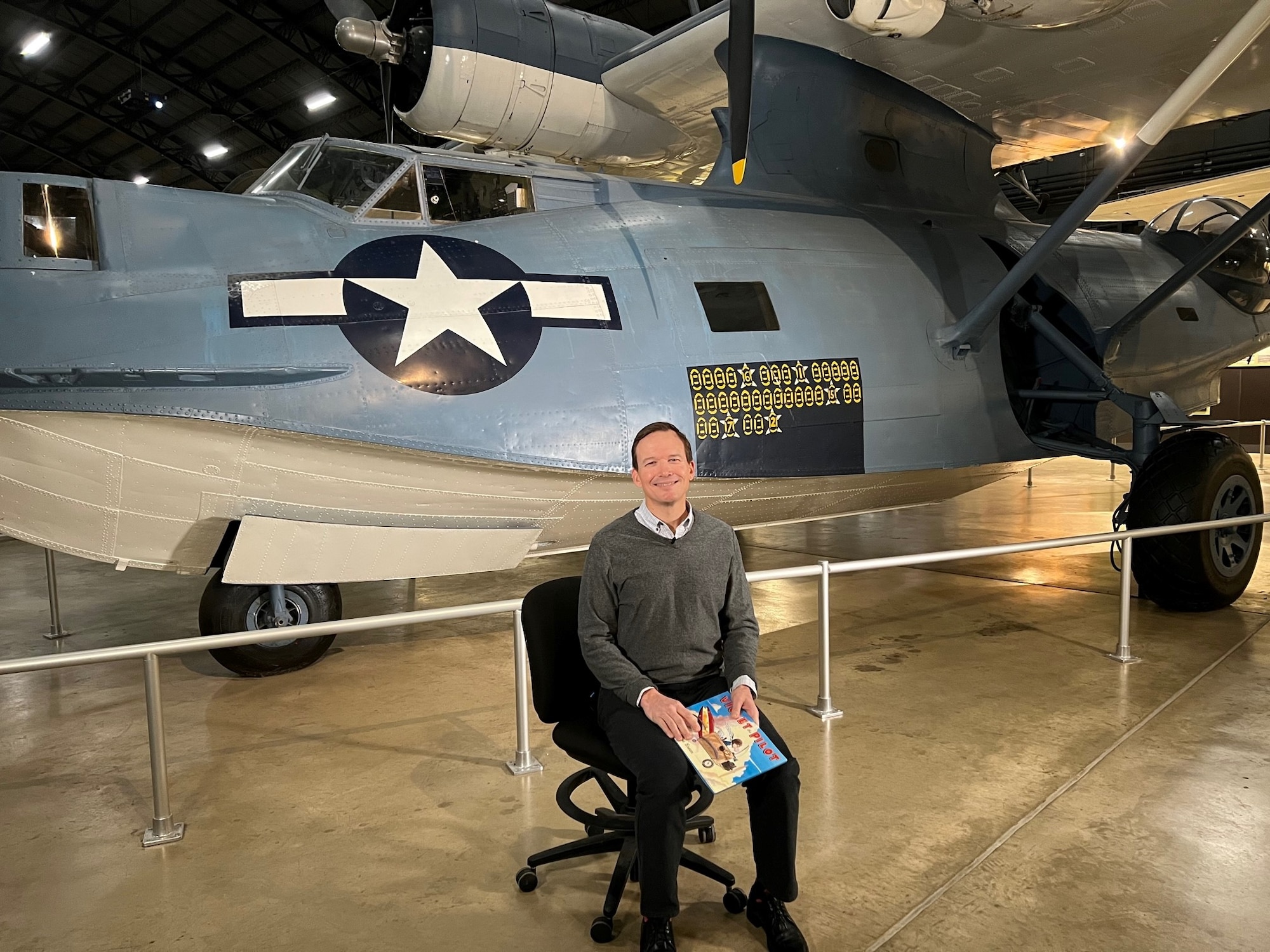 Guest reader sit in front of aircraft in the museum as they read books for virtual Read Across America.