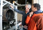 Dr. Tom Jenkins, left, president of MetroLaser, Inc., explains to Dr. David Mayo, with the Naval Air Warfare Center Aircraft Division, how the cameras are adjusted to best capture the particulates of exhaust from an aircraft engine during a break in testing of the measurement system Nov. 18, 2021, at the Propulsion Research Facility.