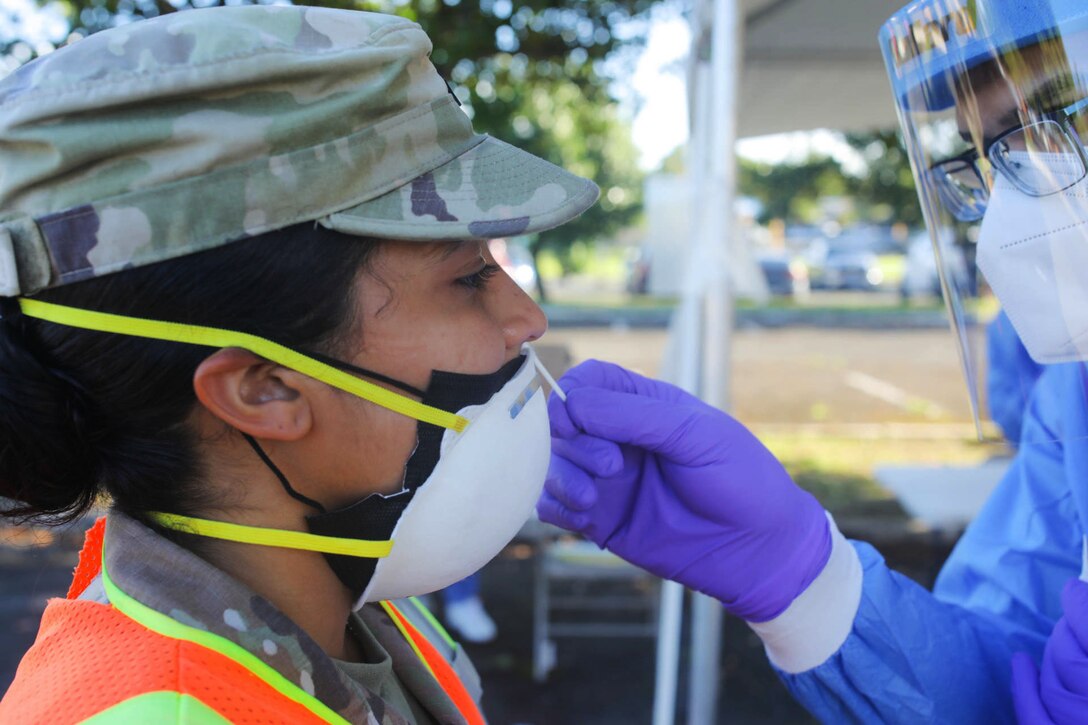 A soldier wearing personal protective equipment administers a COVID-19 test to another soldier.