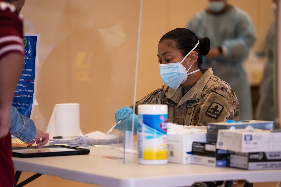 A soldier wearing a face mask and gloves sits at a table.