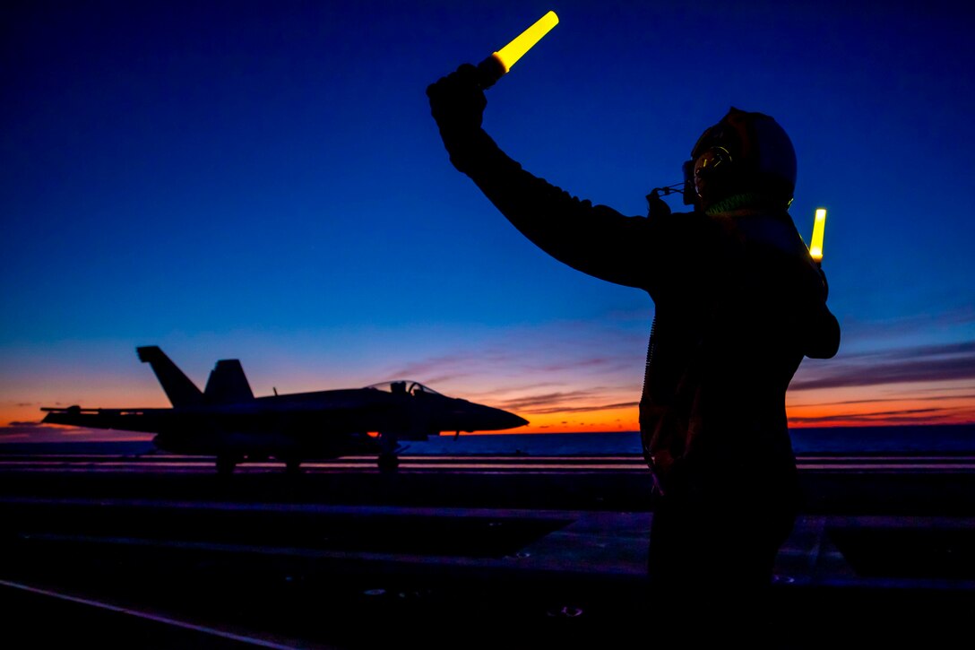 A sailor uses lights to signal toward an aircraft.