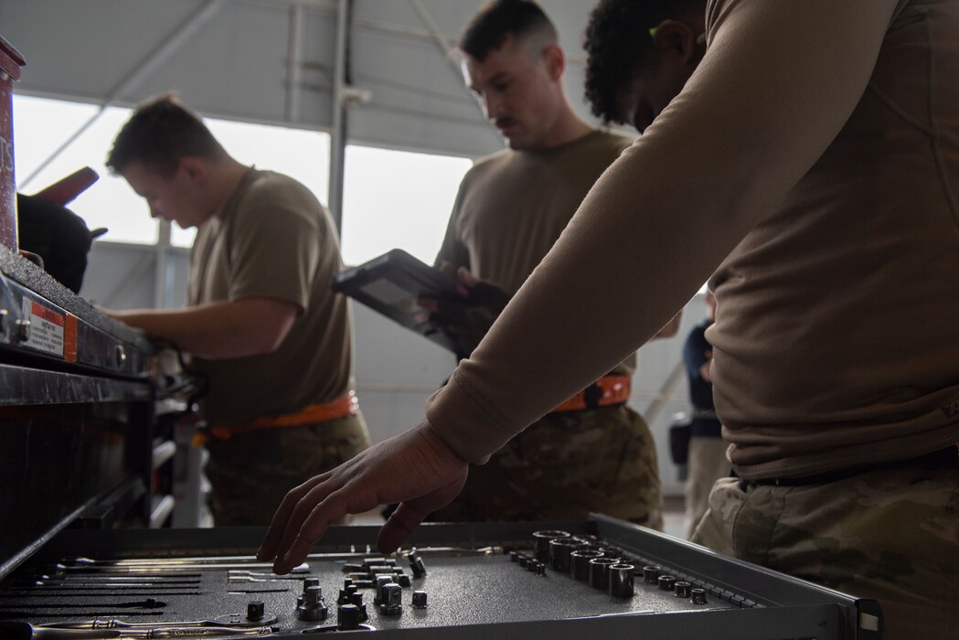 Multiple airmen stand at toolbox to take inventory and put away tools.