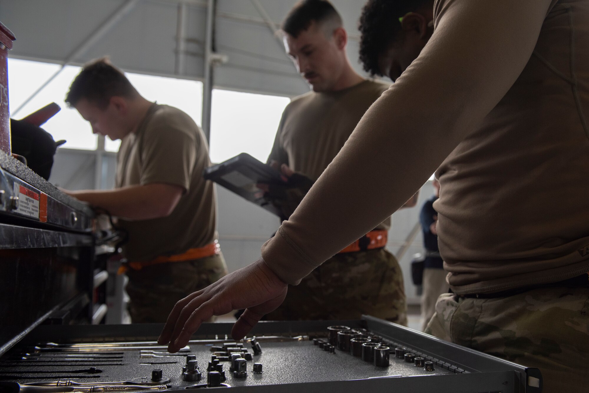 Multiple airmen stand at toolbox to take inventory and put away tools.