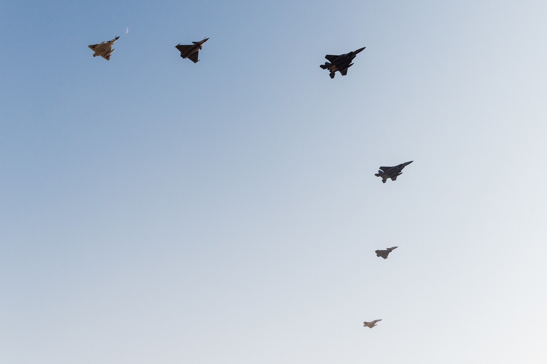 Multiple military aircraft fly in formation against a blue sky.