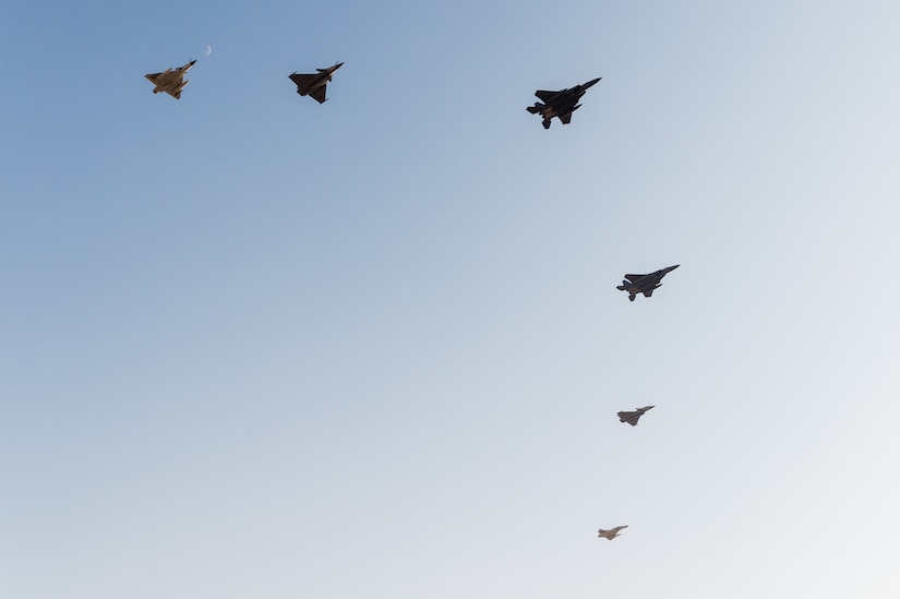Multiple military aircraft fly in formation against a blue sky.