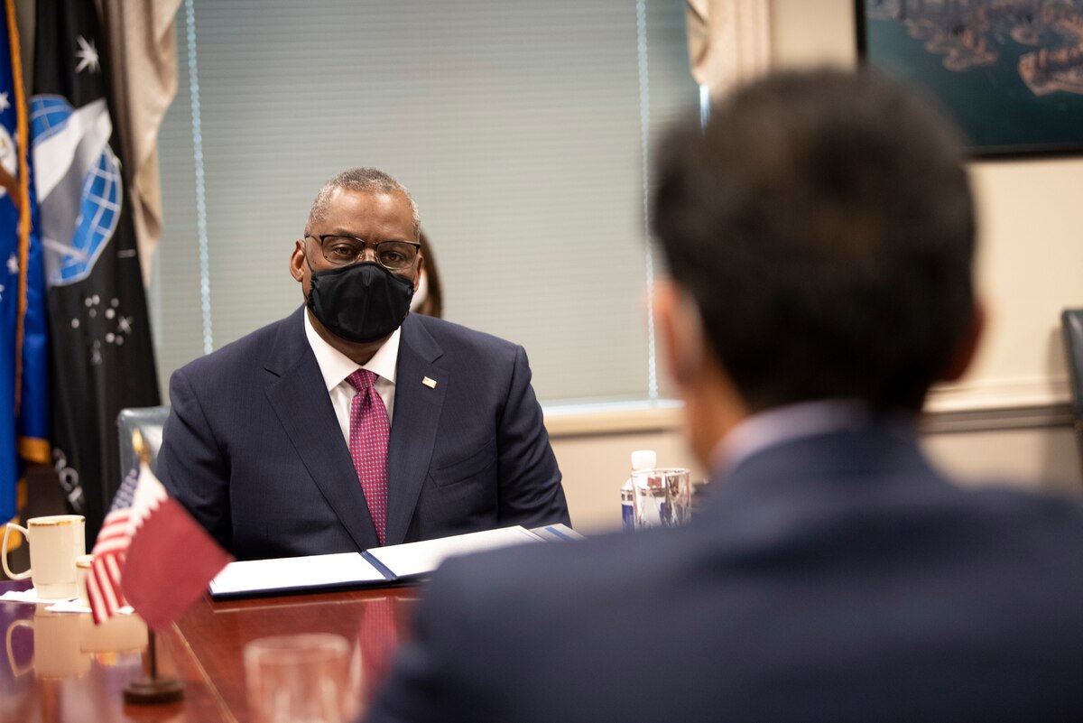 Secretary of Defense Lloyd J. Austin III sits and talks to another official at a table.