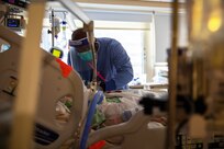 A soldier wearing personal protective equipment monitors a patient’s breathing.