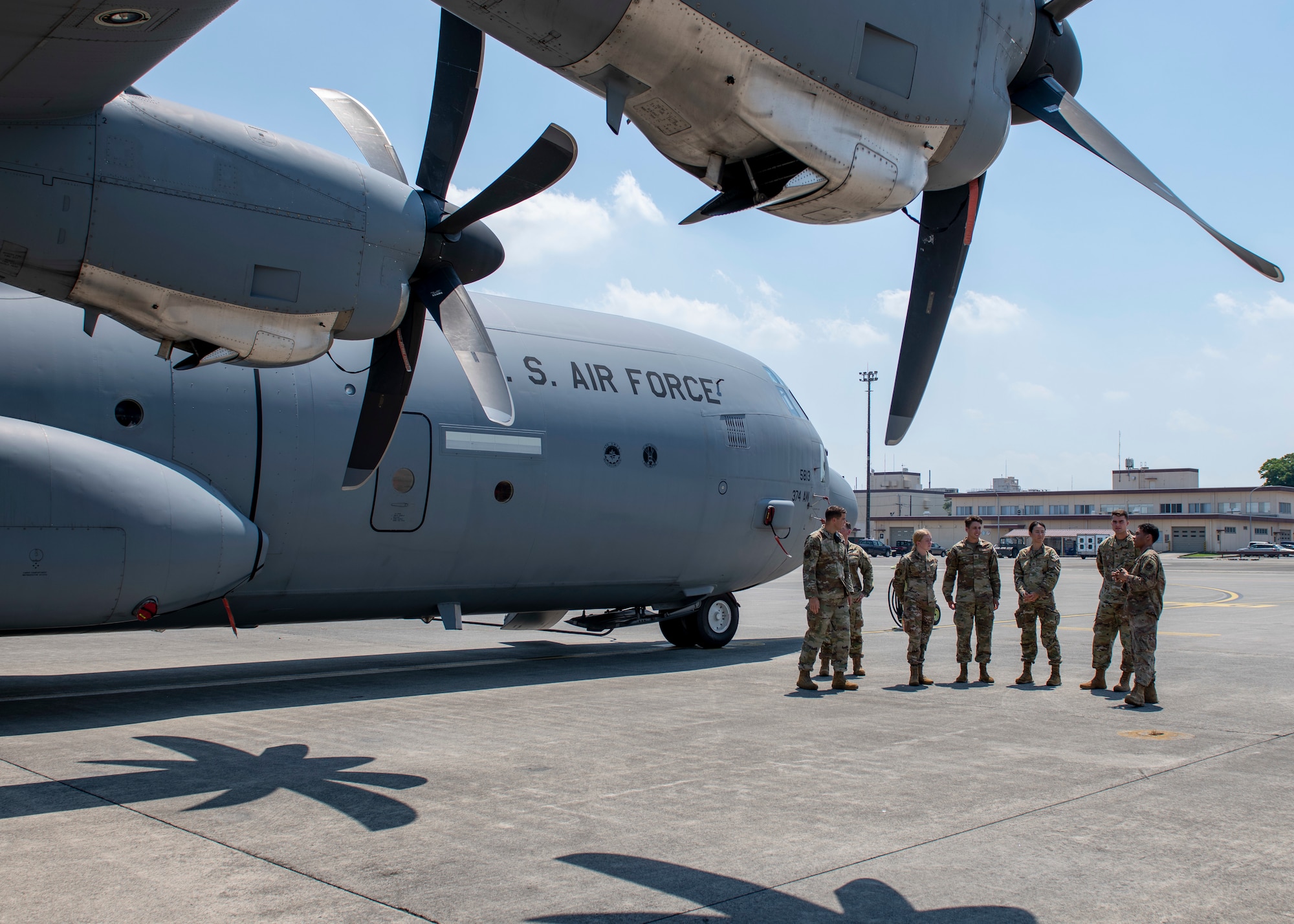 Seven uniformed people stand under a large cargo plane wing.