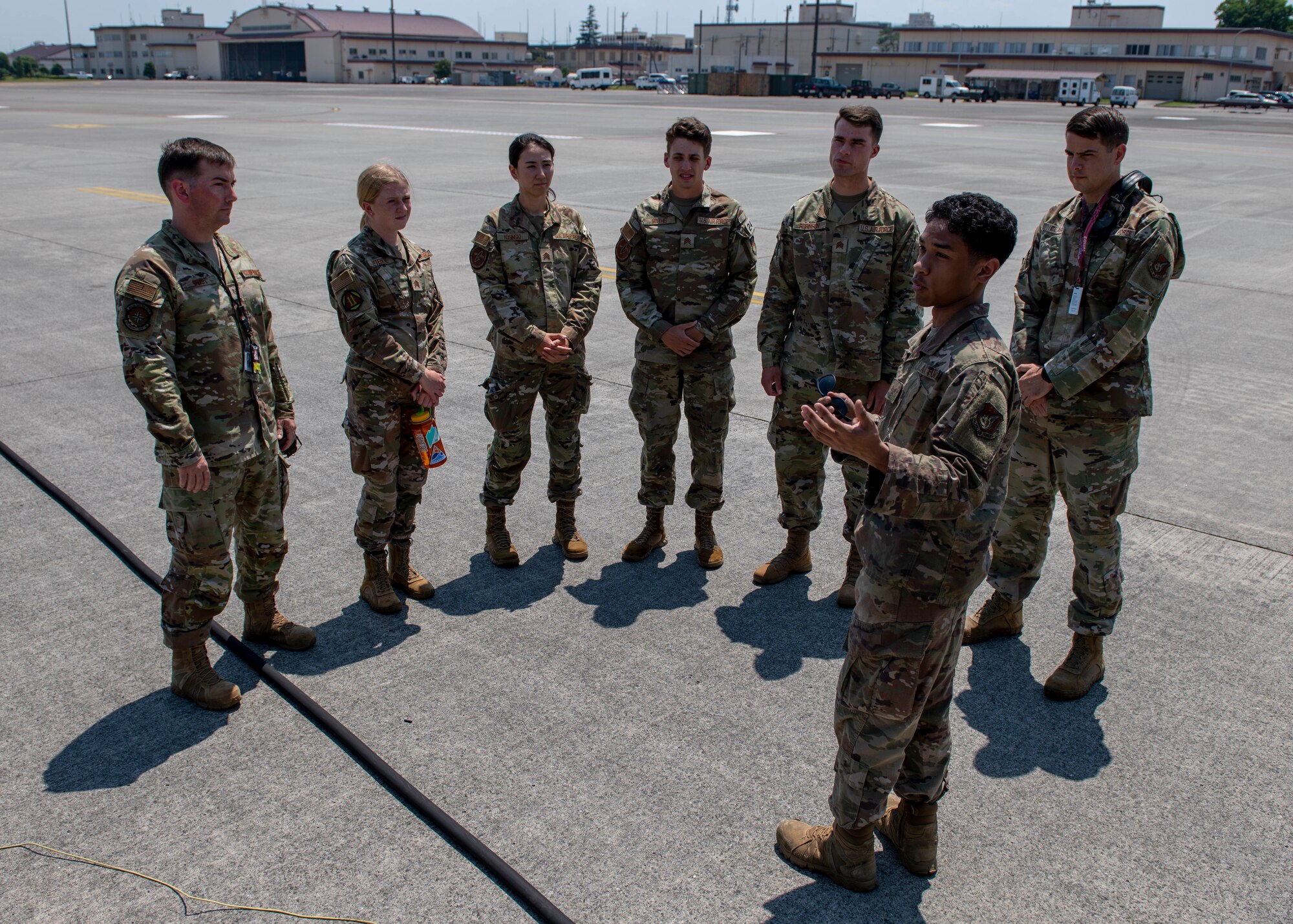 A sergeant gestures to an aircraft while six uniformed cadets look on.