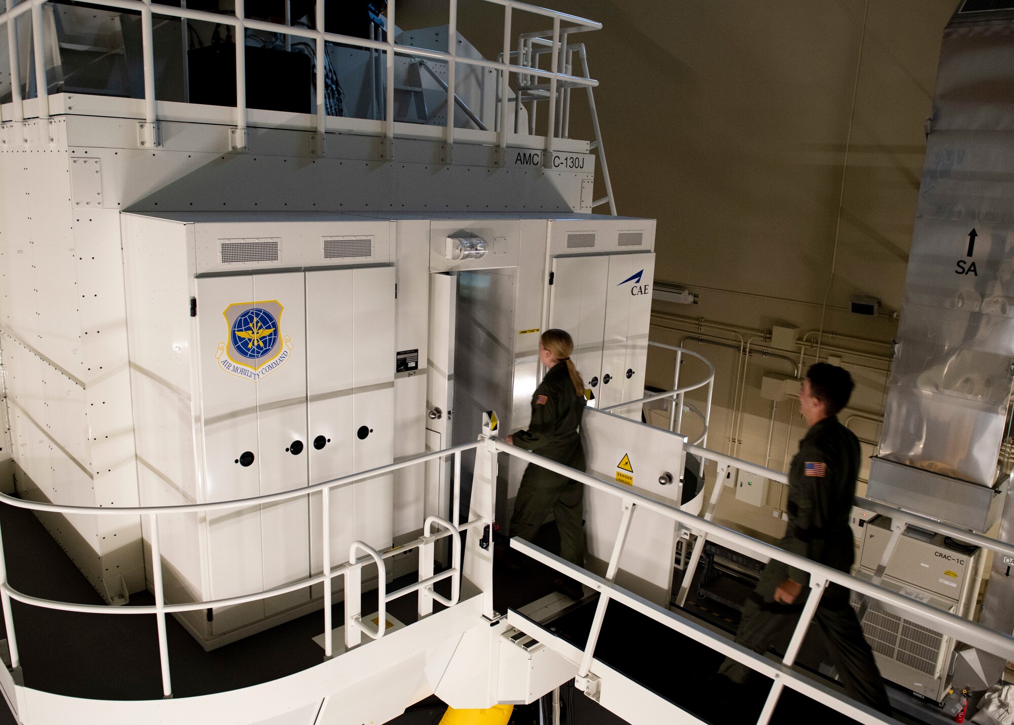 Two cadets in pilot uniforms enter a large white box sitting on hydraulics.