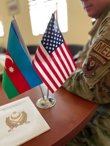 An air adviser with the 137th Special Operations Medical Group, Oklahoma Air National Guard, alongside the flags of the United States and Azerbaijan during a State Partnership Program visit with Azerbaijan Operational Capabilities Concept Battalion doctors and medical noncommissioned officers in Baku, Azerbaijan, conducted June 20-24, 2022. The 137th SOMDG learned how the Azerbaijan military trains its troops for combat medical response and will develop doctrine the Azerbaijan military can use to work toward becoming interoperable with NATO forces.