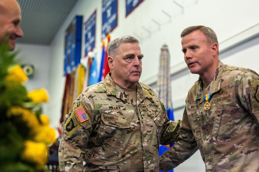 Two men dressed in military uniforms greet one another.