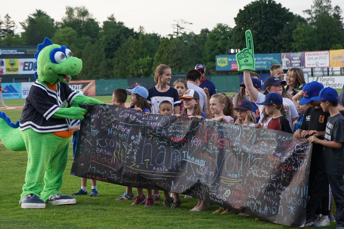 Photo of Lake Monster mascot Champ receiving a Thank You banner from Military Kids during the 7th inning stretch