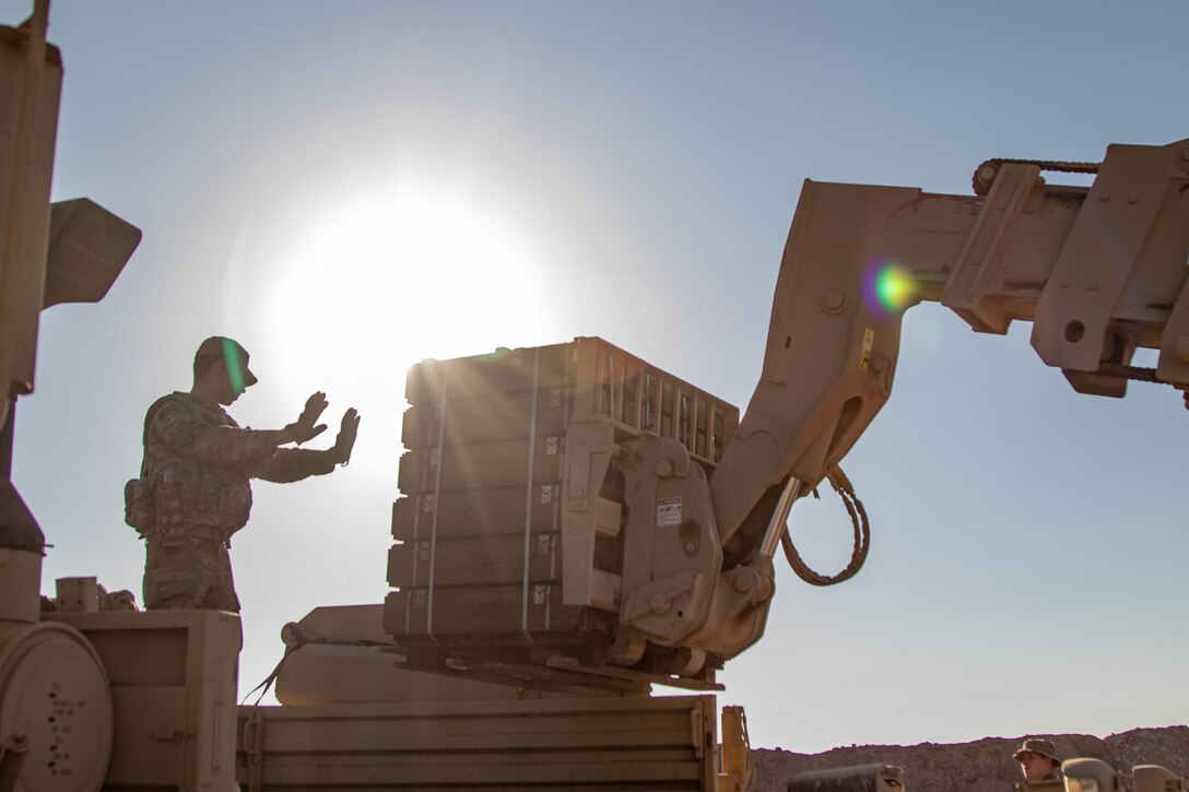 A soldier stands with his arms outstretched next to a large machine.