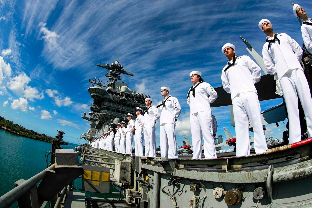 Sailors stand in formation on the rails of a ship.