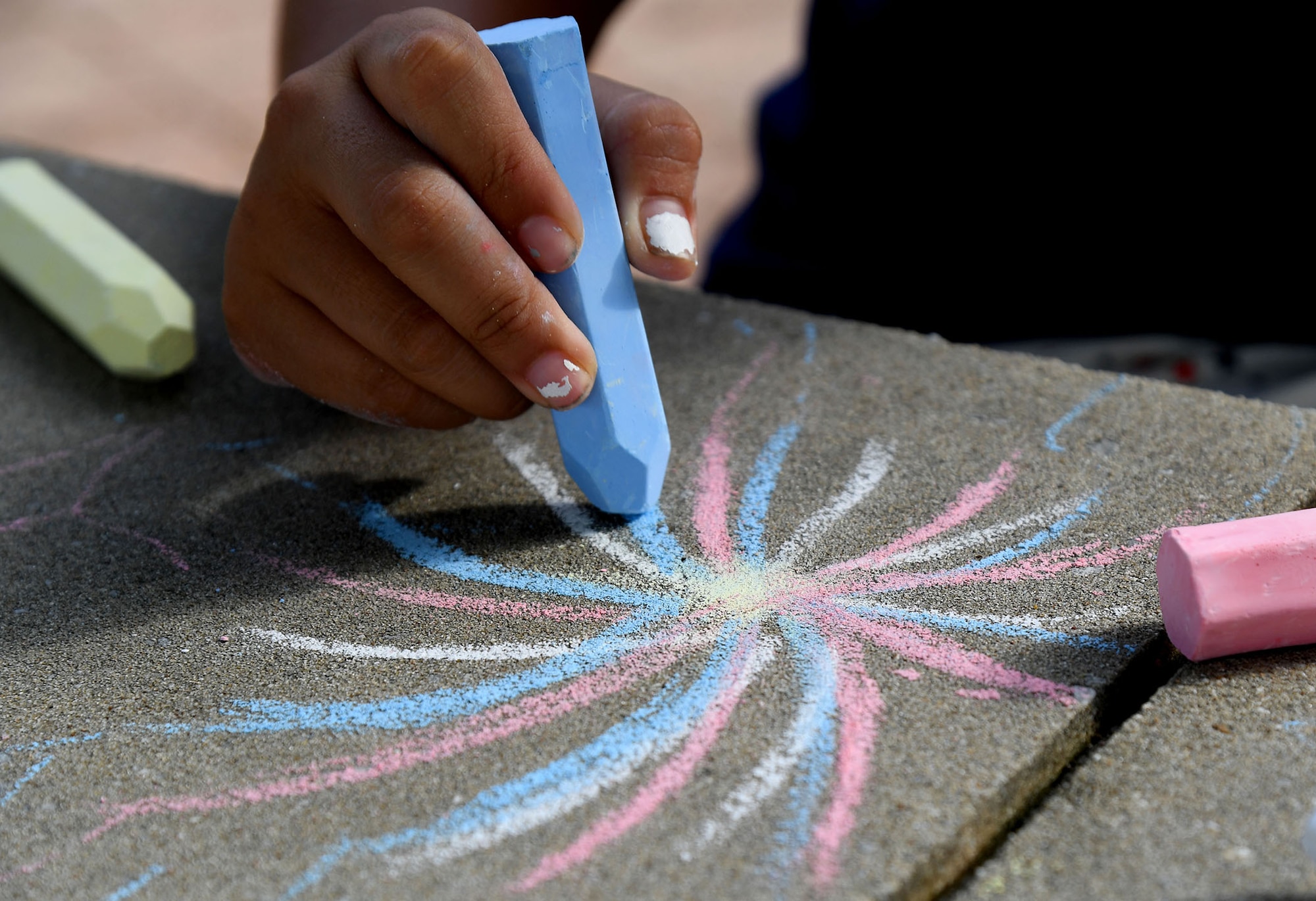 Alexandra Garcia, daughter of U.S. Navy Petty Officer 2nd Class Bonicio Garcia, Naval Mobile Construction Betallion Center 1 Construction Mechanic, Gulfport, Mississippi, draws a firework with chalk during Freedom Fest at the Bay Breeze Event Center on Keesler Air Force Base, Mississippi, June 30, 2022. The event included a hot wing eating contest, a frozen mullet toss competition and fireworks. (U.S. Air Force photo by Kemberly Groue)