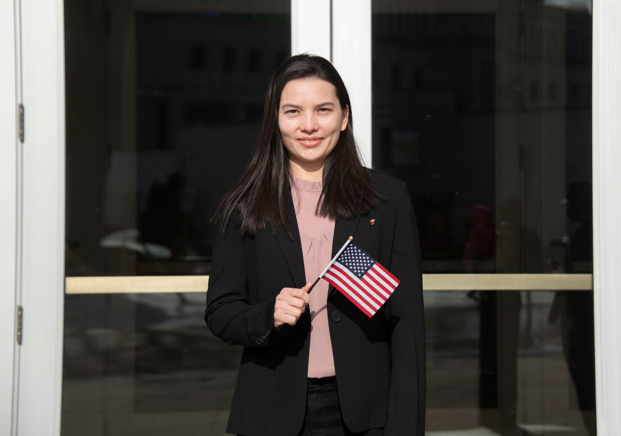 Airman 1st Class Lian Espinoza Fuentes, 319th Force Support Squadron food services journeyman, holds an American flag in front of Barry Hall at North Dakota State University on March 9, 2022, in Fargo, North Dakota. Espinoza Fuentes became an American citizen during a naturalization ceremony in the Barry Hall auditorium. (U.S. Air Force photo by Senior Airman Dakota C. LeGrand)