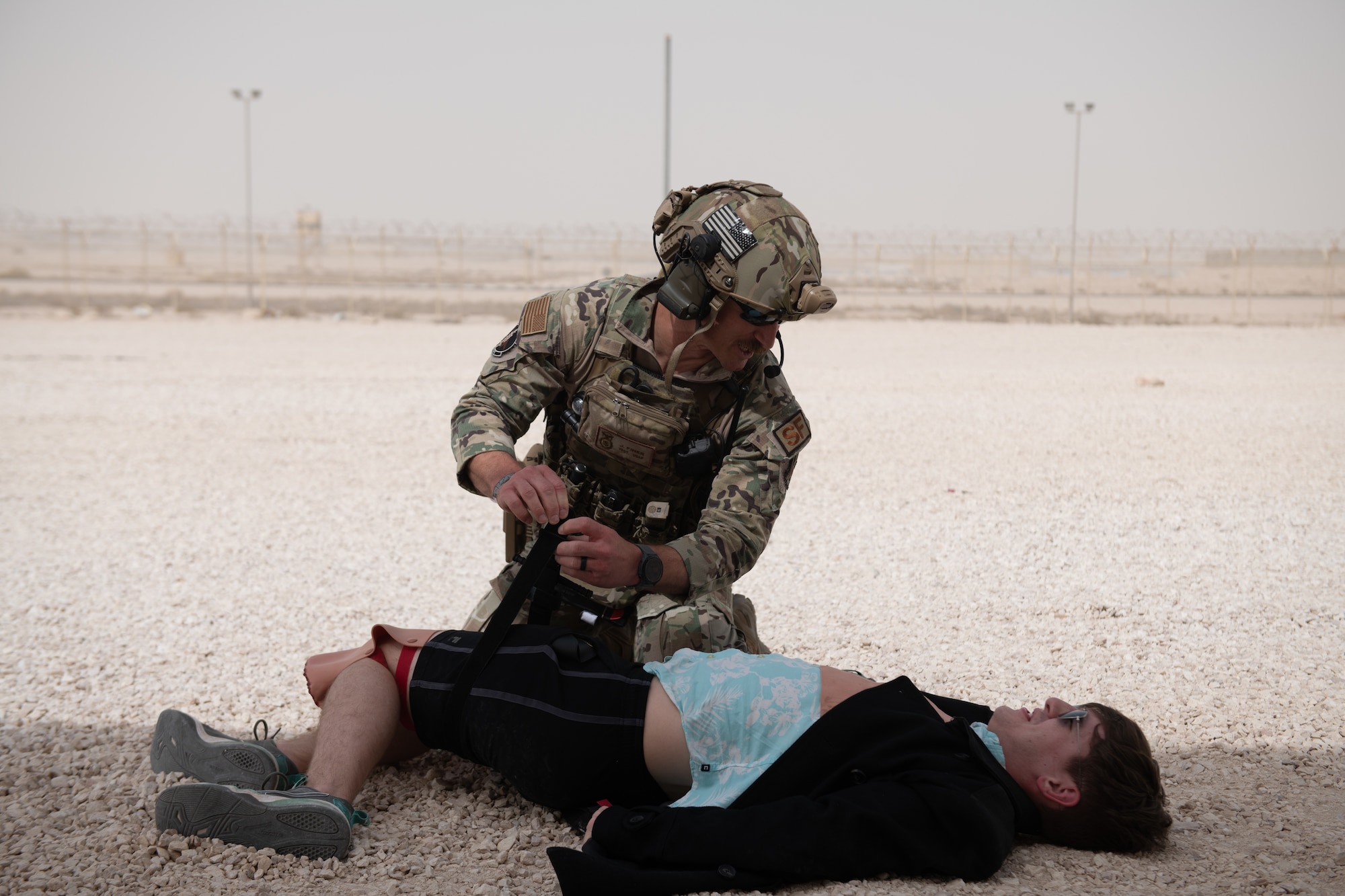 U.S. Air Force Tech. Sgt. Johnathan Finer, a security forces member with the 379th Expeditionary Security Forces Squadron, keeps a simulated casualty awake and engaged whilst applying a tourniquet to a simulated leg injury on Al Udeid Air Base, Qatar, June 27, 2022. Tourniquets are used to treat heavily bleeding limb injuries. (U.S. Air National Guard photo by Airman 1st Class Constantine Bambakidis)