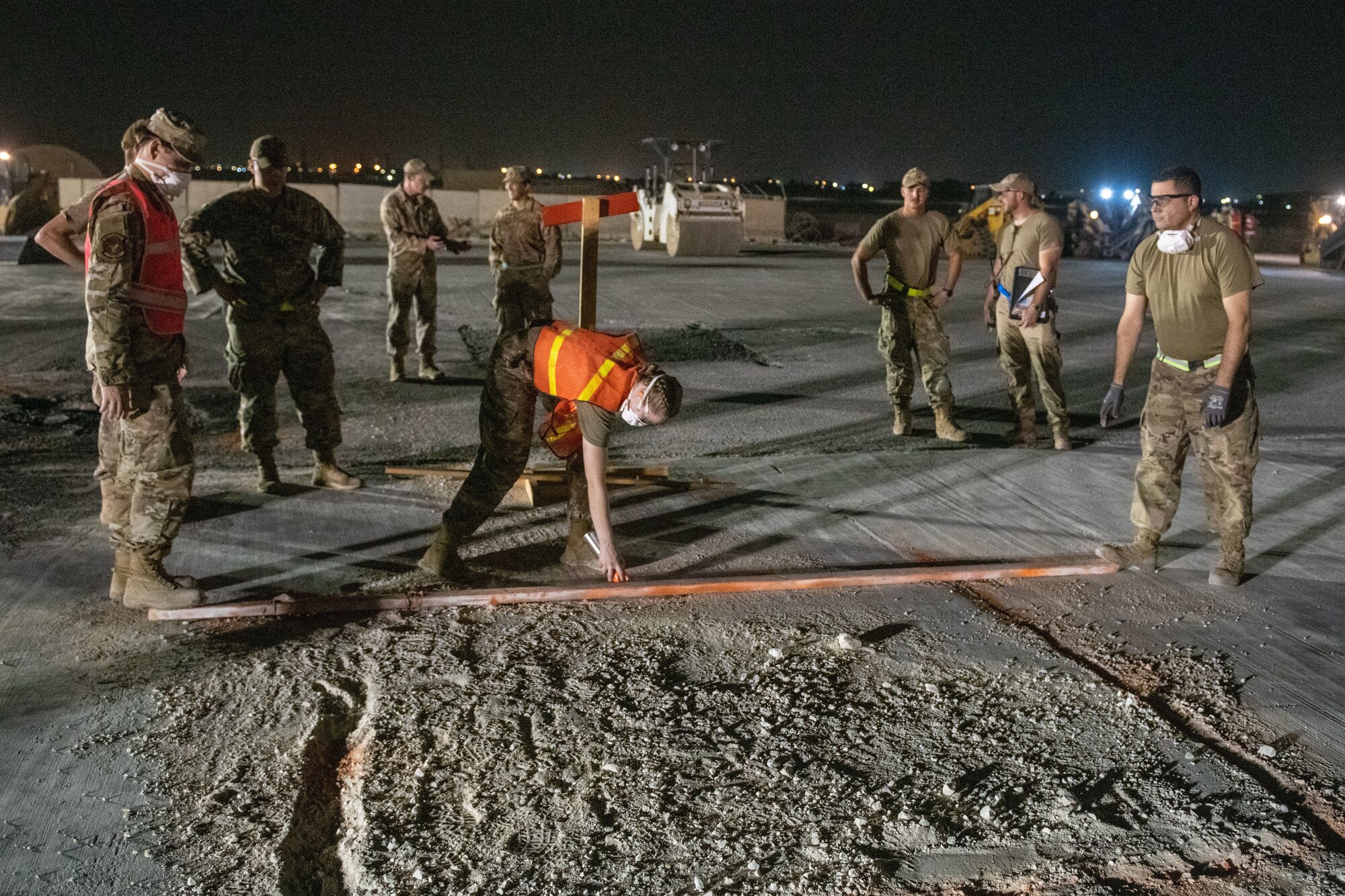 U.S. Air Force engineer assistants with the 379th Expeditionary Civil Engineer Squadron spray orange lines on the pavement surrounding a crater during a flight line repair exercise on Al Udeid Air Base, Qatar, June 27, 2022. The crater is extracted using heavy machinery, then replaced. (U.S. Air National Guard photo by Airman 1st Class Constantine Bambakidis)