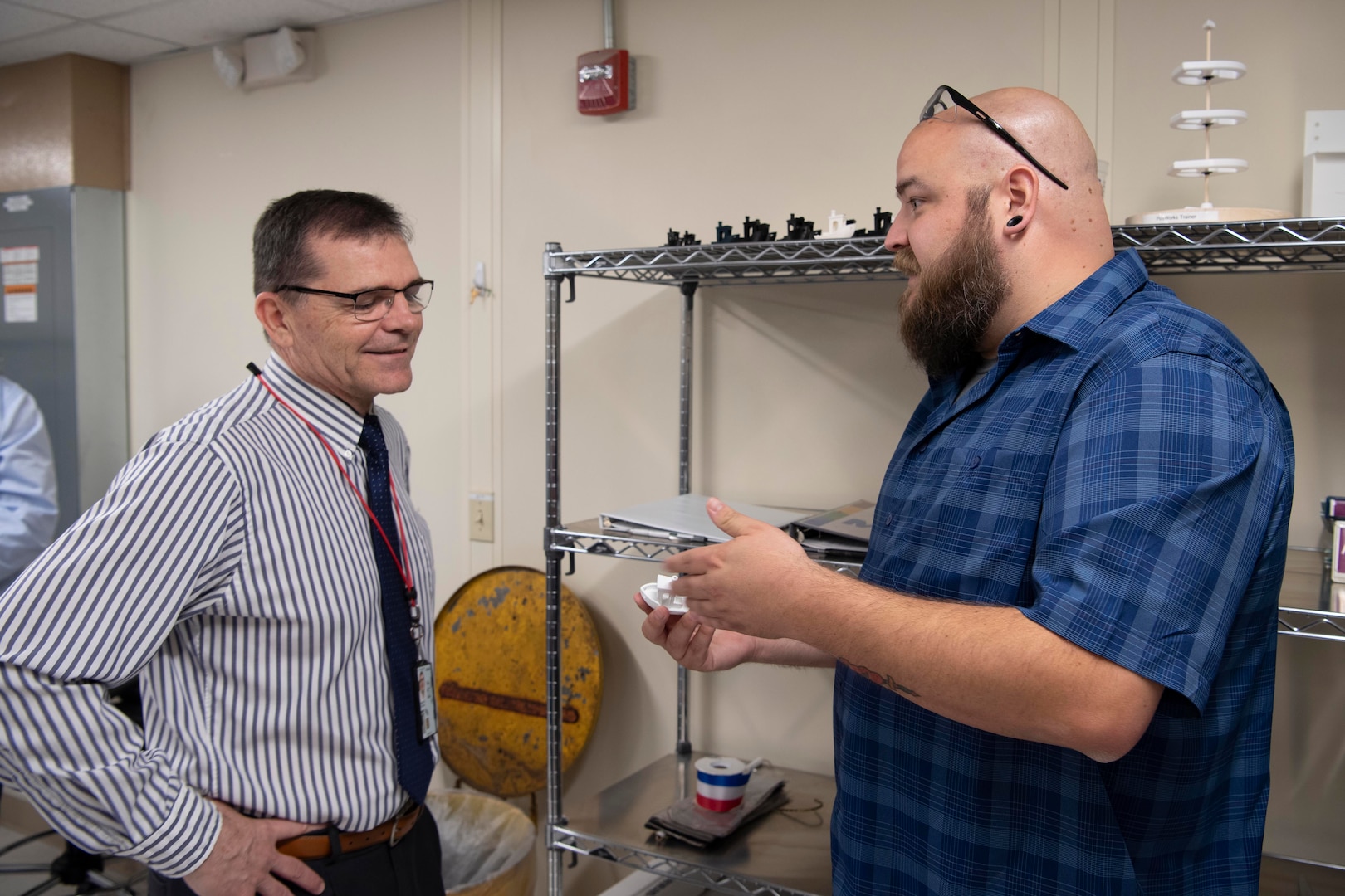Ryan Franke (right), a technician in Carderock’s Subtractive and Additive Manufacturing Branch, explains to Steve Ouimette, Carderock’s Deputy Technical Director, what Benchy the Tug Boat is and what it is used for, during the grand opening of Carderock’s new Advanced Manufacturing Prototyping (AMP) Lab. Benchy, or Benchmark, is the 3D printed part that Franke is holding. Benchy is a quick, little test part that was created to test the limits of a 3D printer. It was designed with a few features that are known to be difficult obstacles for 3D printers. Here, Franke explains that Benchy is used in the AMP Lab training class to allow new users the opportunity to get in the Driver’s Seat and learn start to finish how to create a Build Platform for the Printers, and how to get that platform from the computer to the printer itself and how to get the print started. (U.S. Navy photo by Devin Pisner)