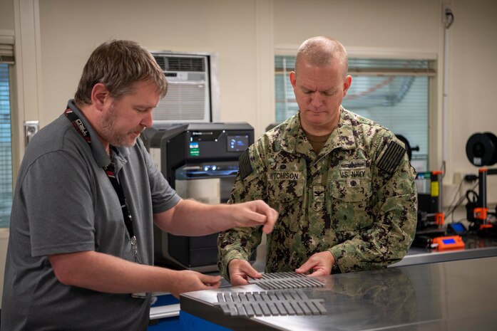 Dr. John Sterling, an engineer in the Emergent Technology and Signature Analysis Branch at Naval Surface Warfare Center, Carderock Division, shows Carderock Commanding Officer Capt. Todd Hutchison fabricated vibration absorbers on June 23, 2022, during the grand opening of Carderock’s new Advanced Manufacturing Prototyping (AMP) Lab. Sterling did his dissertation in 2020 on this research and had used additive manufacturing to develop the prototype before having them machined for testing onboard ships. (U.S. Navy photo by Devin Pisner)