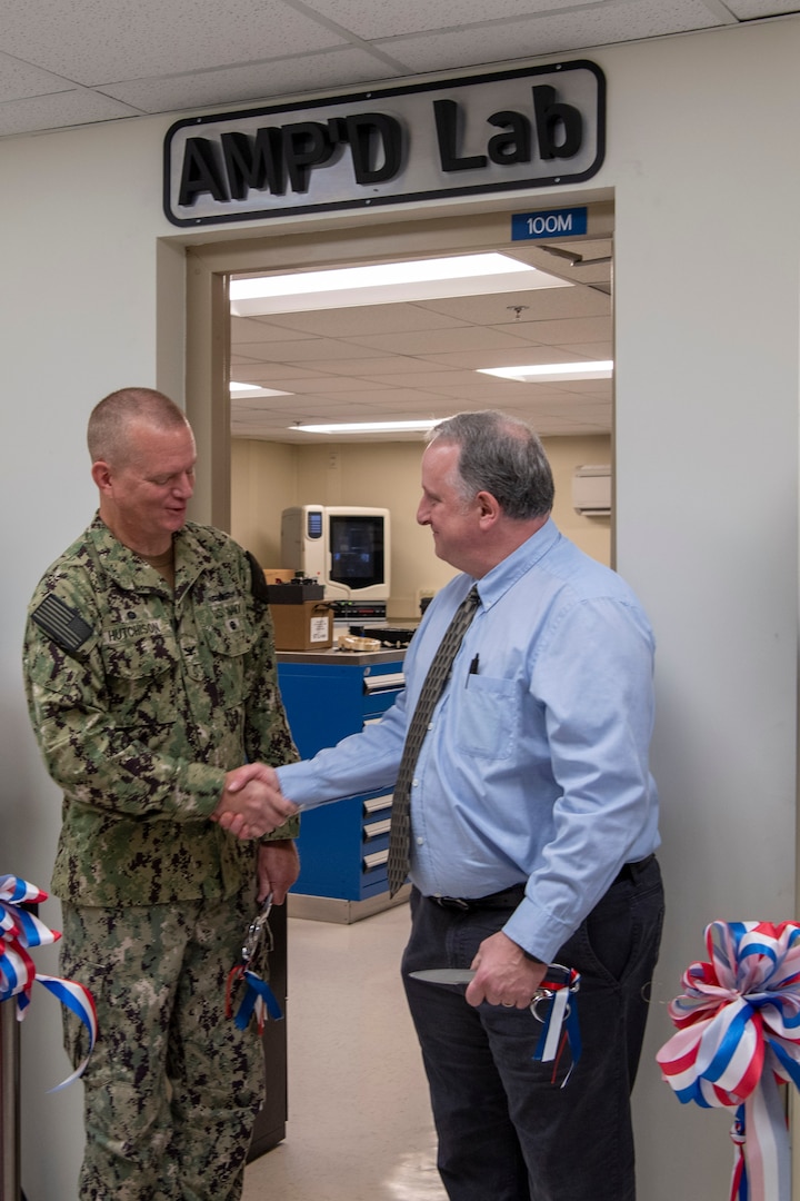 Naval Surface Warfare Center, Carderock Division’s Commanding Officer, Capt. Todd E. Hutchison and Paul Young, Head of the Fabrication and Technical Support Division, shake hands after cutting the ribbon during the grand opening of Carderock’s new Advanced Manufacturing Prototyping (AMP) Lab on June 23, 2022. The AMP Lab is located in Carderock’s Model Fabrication Facility in Building 9. Note the AMP’D Lab sign, which was additively manufactured, and hangs above the entrance to the AMP Lab. (U.S. Navy photo by Devin Pisner)