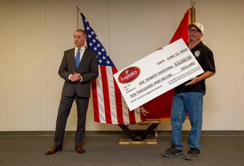 Robert "Chip" Schwartz (left), Production Plant Barstow manager, speaks to the crowd after presenting the $10,000 check to Robert Hartong (right), optics journeyman, for his contributions during the presentation ceremony held on Marine Corps Logistics Base Barstow, California, June 30, 2022. Hartong had developed a piece of glass for the LAV-25 and effectively save the government over $400,000 and was estimated by Schwartz to have saved the Marine Corps over a million dollars, with a prediction of several more millions of dollars saved. (U.S. Marine Corps photo by Jack J. Adamyk)