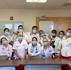Group of nursing students in medical garb pose around a table