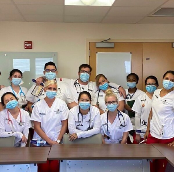 Group of nursing students in medical garb pose around a table