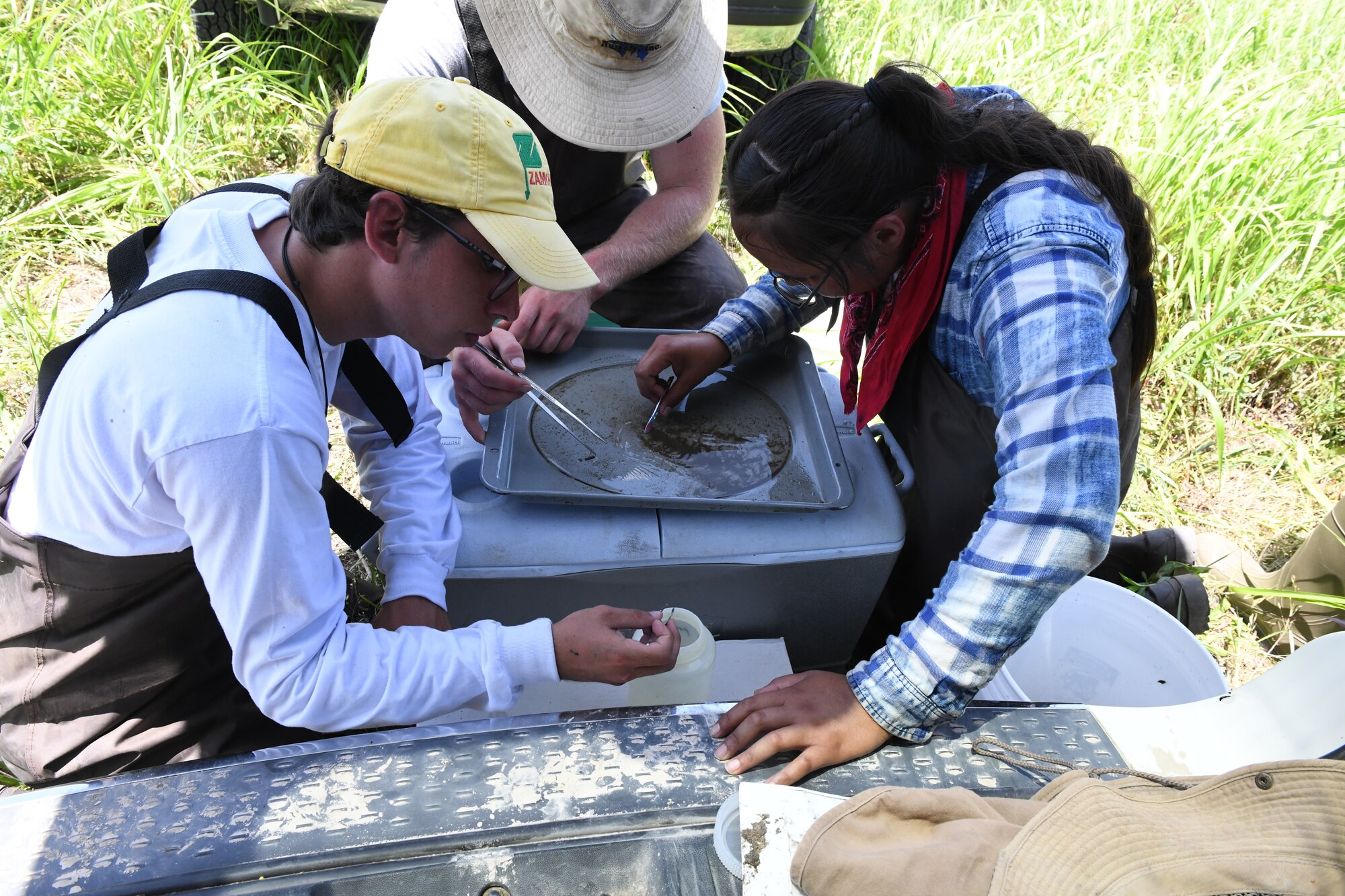 Kansas State University students Jorge Serrana (left), Josh Wurtz (center) and Daryline Dayzie painstakingly collect splinter-sized invertebrates from McConnell Creek on June 16, 2022, at McConnell Air Force Base, Kansas. The collection assessed the health of the river's aquatic population base before the KSU team began modifications to the creek's shoreline as part of their erosion control study. The McConnell portion of this KSU study is part of a partnership between KSU, the U.S. Fish and Wildlife Service, and McConnell Air Force Base. (U.S. Air Force photo by John Van Winkle)