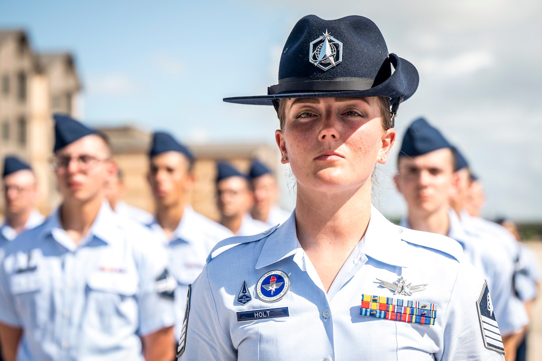 A guardian military instructor stands at the front of a formation of guardians at an outdoor ceremony.